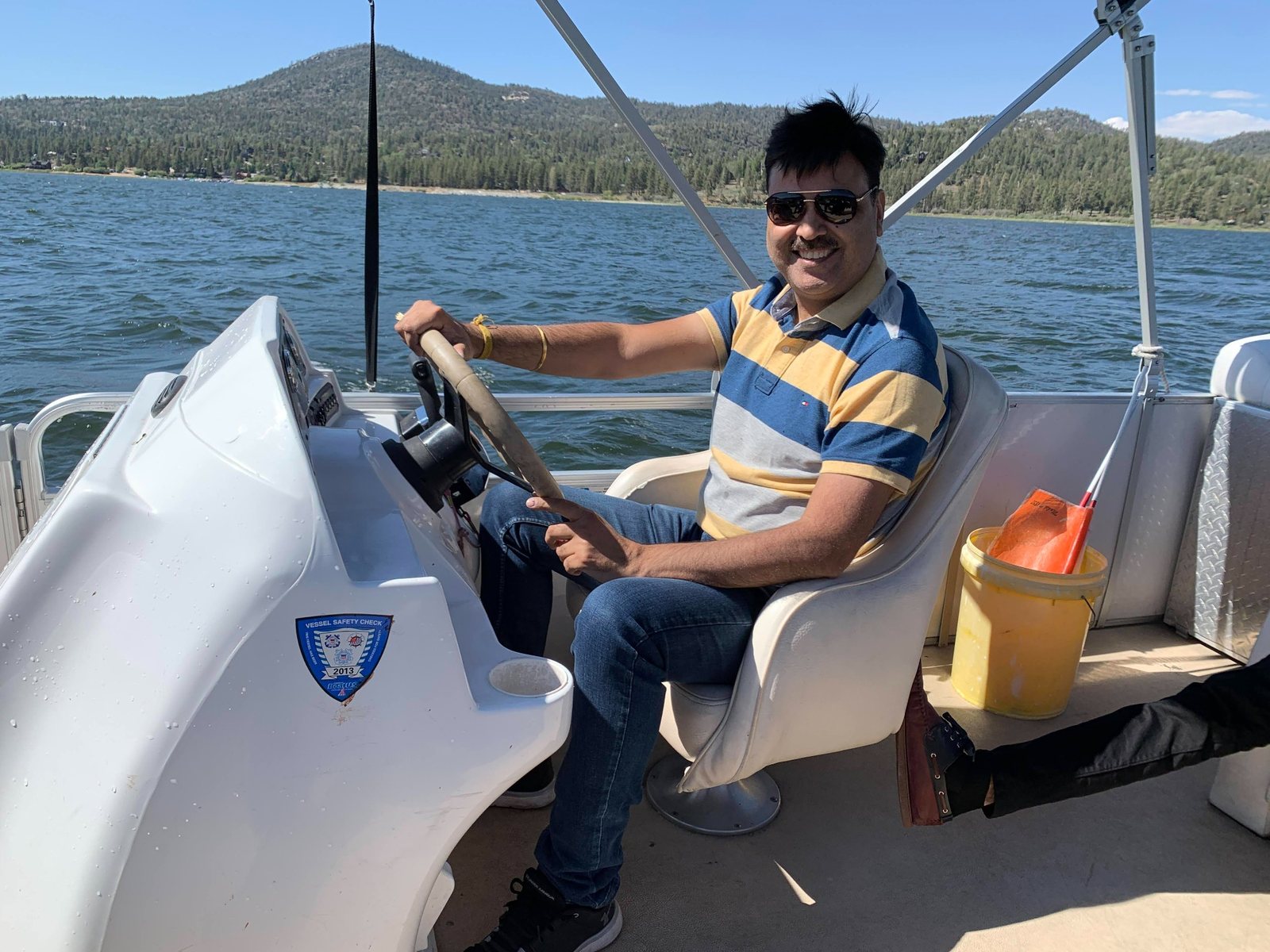 Gaurav Ghulati smiling while steering a boat on a lake.